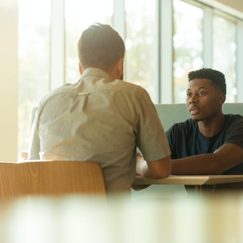 two-men-talking-while-sitting-beside-table-1251860